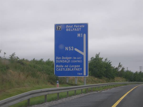 Blue M1 road sign to Belfast and Dundalk under grey sky