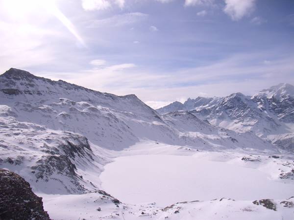 Frozen lake surrounded by snowy peaks under a cloudy sky