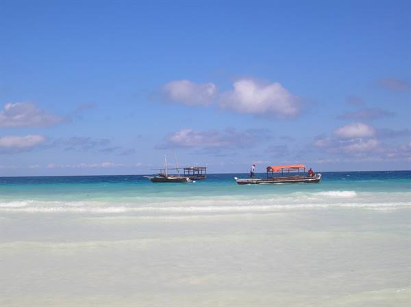 Wooden boats float on turquoise water in front of white sand beach