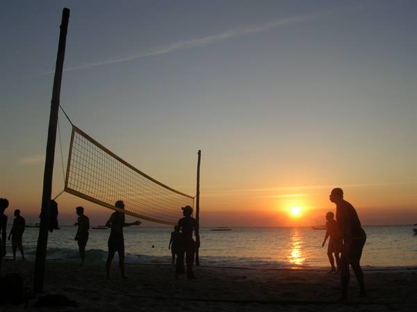 People playing beach volleyball on sandy shore at sunset