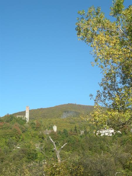 Old stone tower on green hillside under blue sky among autumn trees