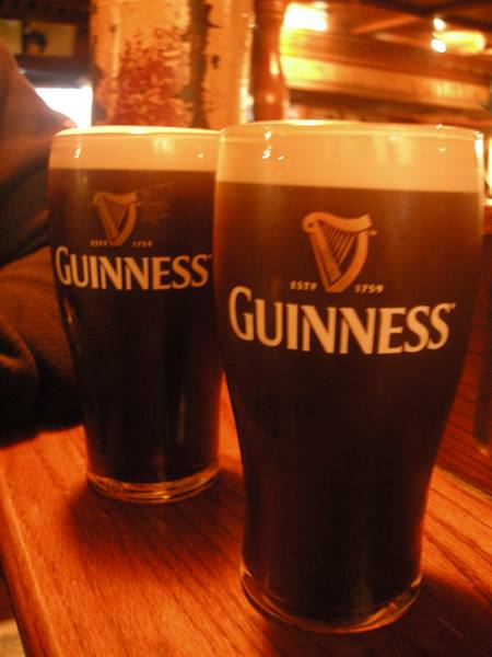 Two pints of Guinness with foam on a wooden pub counter