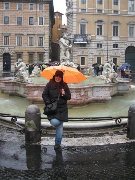 Woman with orange umbrella in front of the Moor Fountain at Piazza Navona, Rome, in the rain