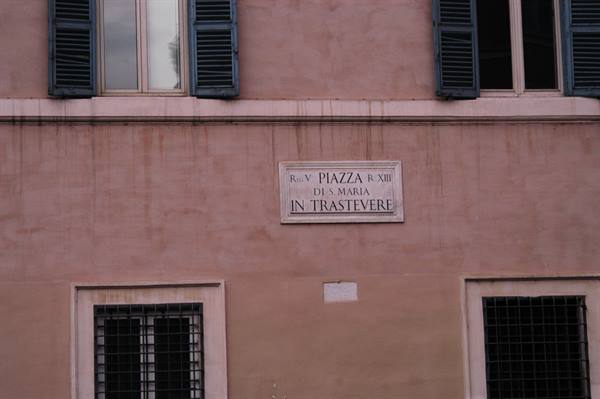 Marble plaque of Piazza de Santa Maria in Trastevere on pink facade with shutters
