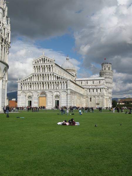 Tourists resting on the lawn in front of Pisa Cathedral and the Leaning Tower
