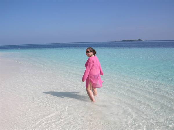 Woman in pink tunic walks through turquoise water on white sand
