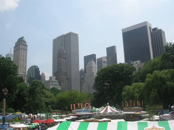 Amusement fair with carousel and green tents beneath Central Park skyline, New York