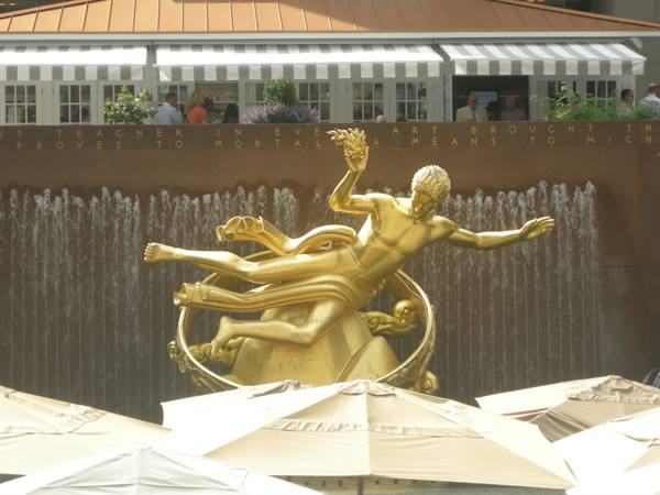 Golden Prometheus statue before the Rockefeller Center waterfall, beige umbrellas below