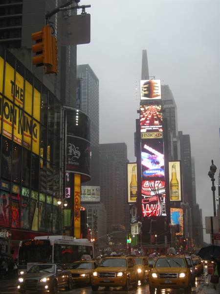 Yellow taxis under glowing billboards in Times Square on a gray day