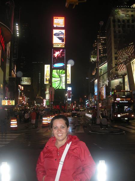 Smiling woman in red jacket on Times Square at night among glowing billboards