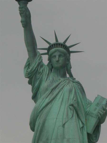 Statue of Liberty, green copper, raising torch against gray sky