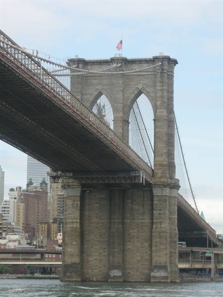 Brooklyn Bridge stone tower with American flag, seen from the water