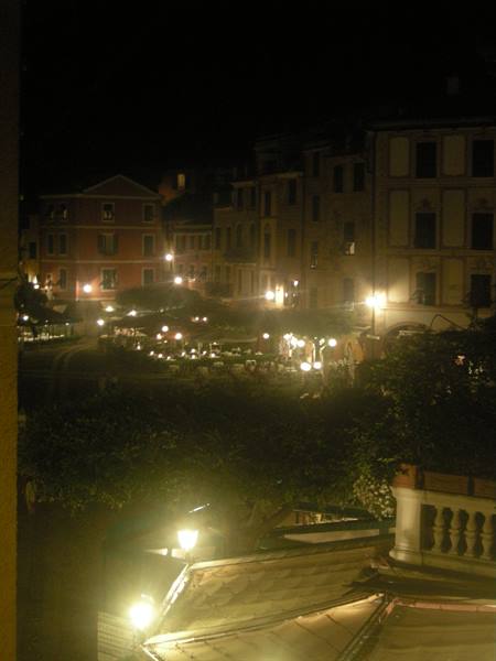 Night square with lit café tables among historic buildings and yellow streetlamps
