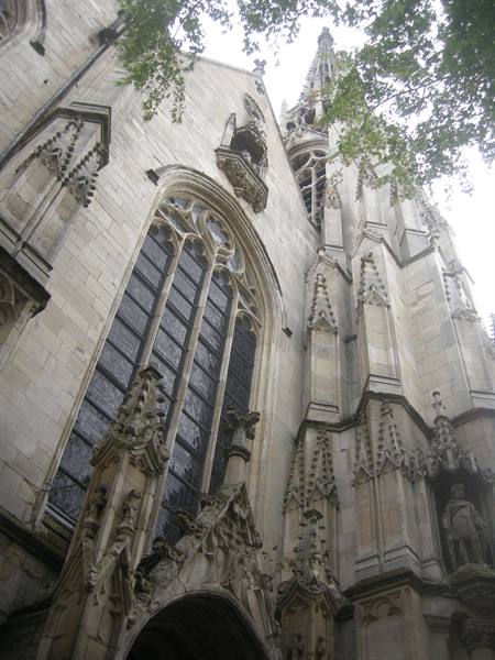 Gothic stone facade with tall tracery window and spire framed by trees