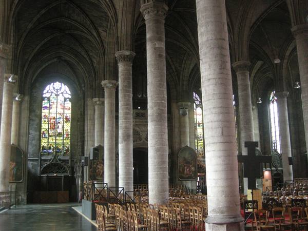 Gothic church interior: stone columns, wooden chairs, stained glass windows filtering light