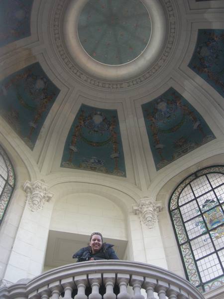 Woman on stone balcony beneath a painted dome with art nouveau windows