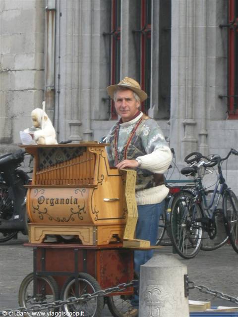 Barrel organ player with toy monkey, bicycles and gothic building behind