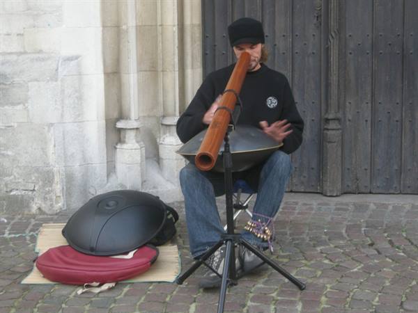 Busker playing didgeridoo and handpan on cobblestones by a wooden door