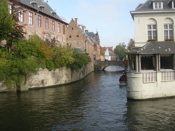 Bruges canal with tourist boat, stone bridge and brick houses