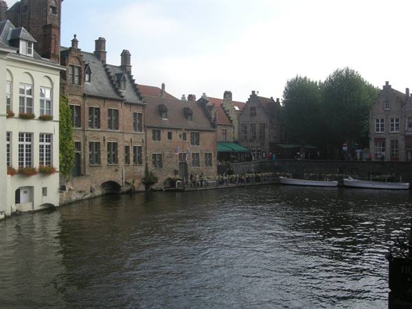 Medieval brick houses along Bruges canal, moored boats under grey sky