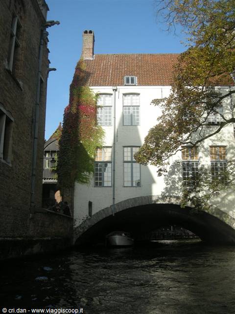 White house with red ivy above a stone bridge on a Bruges canal