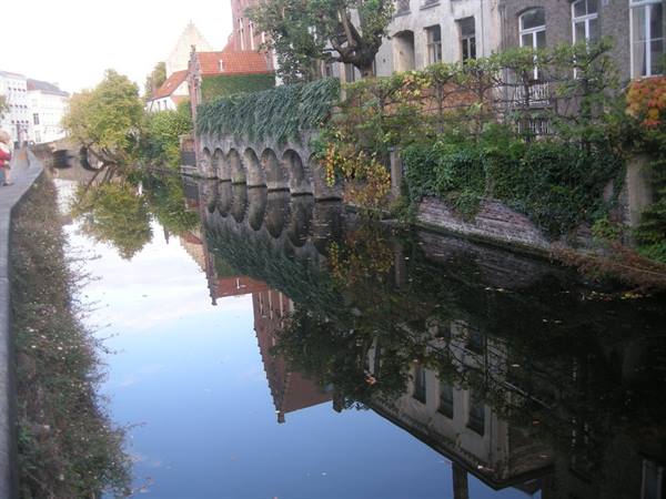 Bruges canal, stone arches and old houses reflected in still water