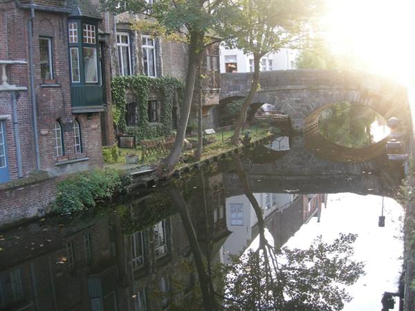 Brick houses along a canal, stone bridge reflected in the water in Bruges
