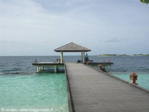 Wooden jetty over turquoise water leading to a thatched pavilion on the sea