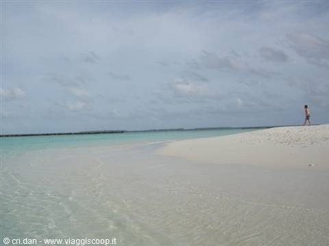 Child walks on white sand, shallow turquoise water and cloudy sky
