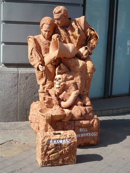 Terracotta street sculpture with skull and jug, 'Gracias' sign, on sunny sidewalk