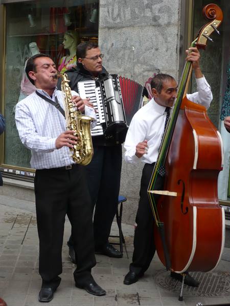 Three street musicians playing saxophone, accordion and double bass outside shops