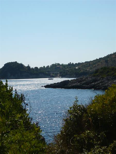Adriatic cove framed by green shrubs, a boat moored on sparkling water