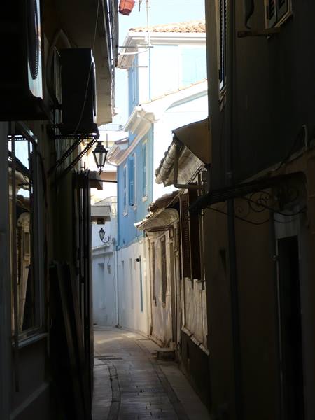 Narrow alley between white and blue houses lit by sunlight