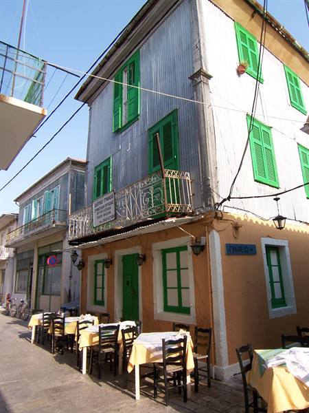Greek tavern with outdoor tables, corrugated metal walls and green shutters