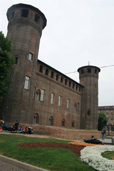 Tourists sitting on the lawn in front of Turin's brick Palazzo Madama