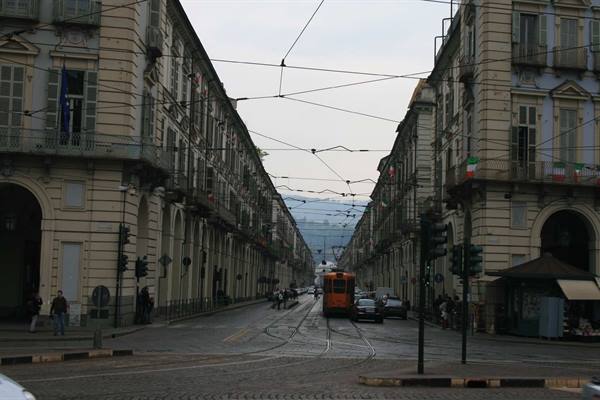 Orange tram in a Turin street between nineteenth-century buildings under wires