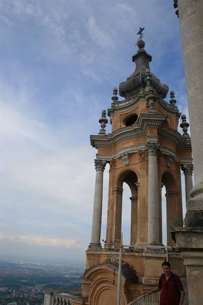 Baroque ochre stone bell tower with columns, cloudy sky, a visitor beside