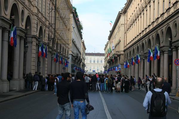 People under the arcades of Via Po, Turin, flags hanging, daylight