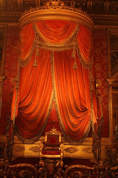 Gilded throne beneath red velvet canopy, royal hall in warm light