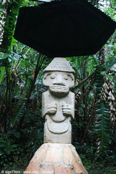 Stone statue at San Agustín under a thatched roof, tropical jungle