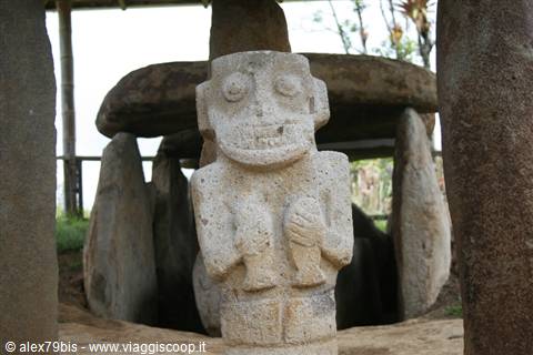 Stone statue at San Agustín Archaeological Park, with megalithic tomb behind