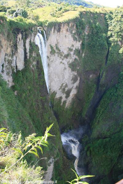 Waterfall plunging down steep green rock cliffs into Sipi Falls gorge