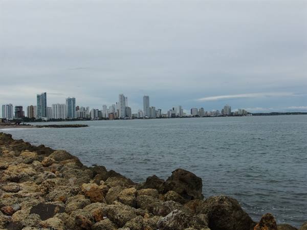 Brown rocky shore in front of Cartagena's skyscrapers under grey sky