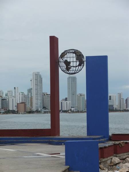 Metal globe monument between red and blue pillars, skyscrapers over the bay
