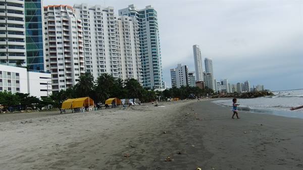 Child walks on the beach beneath skyscrapers and yellow tents in Cartagena