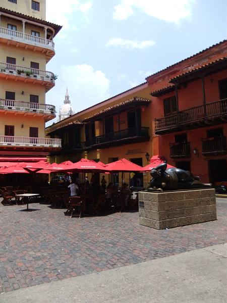 Bronze reclining woman statue on plaza with red umbrellas and colonial balconies