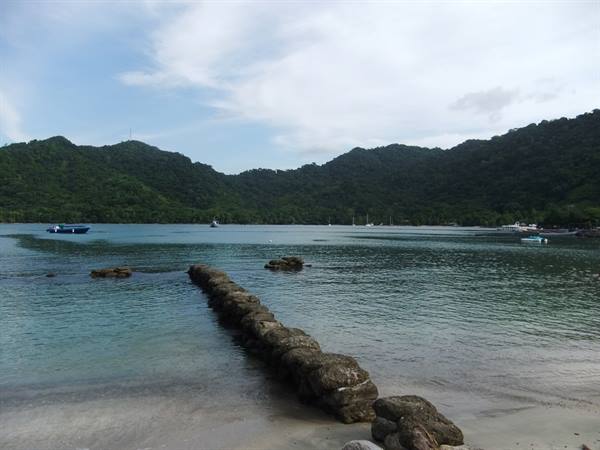 Stone breakwater in a bay, boats and green hills in the background