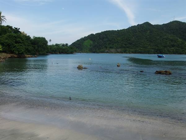 Sandy beach with turquoise water, rocks, boats and lush green tropical hills