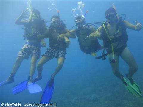 Four scuba divers in gear and fins pose underwater