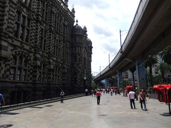 Pedestrians near checkered Palacio de la Cultura, metro pillar in Medellín